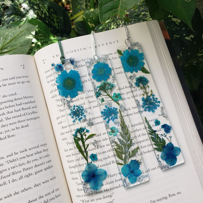 This Blue Floral bookmark design includes a Blue Daisy on top, Blue Queens Lace in the middle, and Blue Hydrangea or another flower at the bottom of the bookmark accompanied by various foliage and silver glitter throughout.