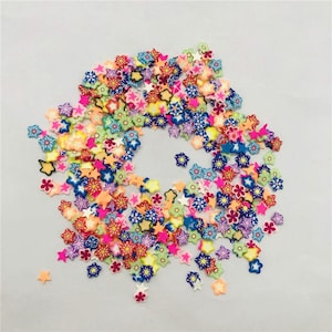 Puede incluir: Un gran surtido de formas de flores y estrellas de arcilla polimérica de colores. Las formas están dispersas sobre un fondo blanco.