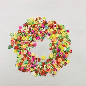 Puede incluir: Un gran surtido de abalorios de arcilla polimérica de colores con forma de fruta. Los abalorios tienen forma de fresas, limones, limas, kiwis, sandías y rodajas de piña.