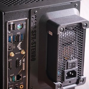 May include: A black computer case with a black and gold motherboard. The case has a power button, a power cord, and a variety of ports, including USB, HDMI, and Ethernet. The case also has a fan on the back.