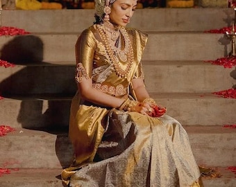Peut inclure: Une femme porte un sari doré et des bijoux en or élaborés, dont un couvre-chef, un collier et des bracelets. Le sari présente une bordure dorée et des motifs complexes. Elle est assise sur des marches en pierre, avec des pétales de fleurs rouges éparpillés.