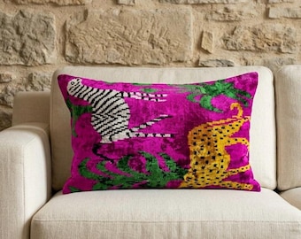 May include: A rectangular decorative pillow with a vibrant fuchsia background. The pillow features a zebra and a cheetah design in black and white, and yellow with green accents. The pillow is placed on a cream-colored sofa.