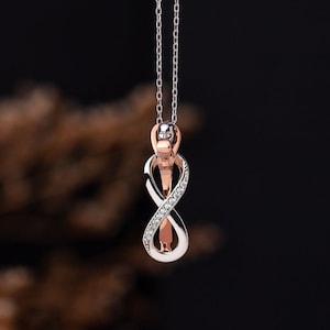 May include: A silver and rose gold infinity pendant necklace with a row of clear cubic zirconia stones.