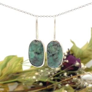 May include: A pair of silver earrings with oval-shaped green emerald gemstones.