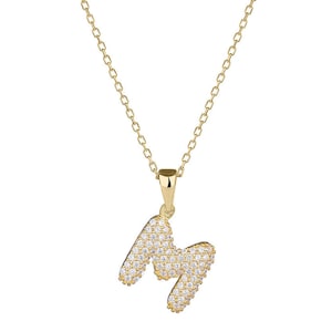 May include: A gold-colored necklace with a pendant in the shape of the letter "M". The pendant is encrusted with small, clear gemstones. The chain is delicate and also gold-colored, hanging against a white background.