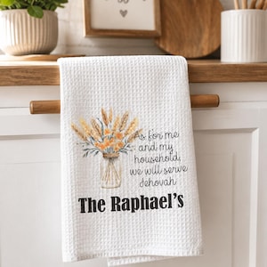 May include: A white waffle-weave kitchen towel featuring a watercolor illustration of wheat and orange flowers in a glass jar. The text reads, As for me and my household, we will serve Jehovah, followed by the personalized name, The Raphael's.