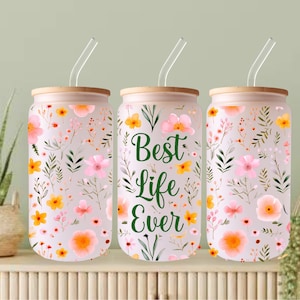 May include: Three reusable glass canisters with bamboo lids and clear straws. The canisters are decorated with a floral pattern in shades of pink, yellow, and green. The middle canister has the text "Best Life Ever" in green lettering.