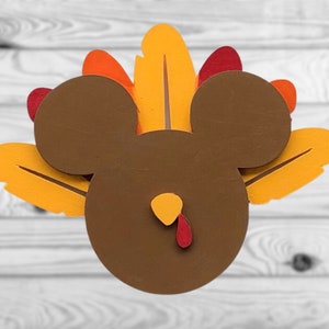 May include: A brown turkey-shaped ornament with a red wattle and yellow feathers. The turkey has a Mickey Mouse head.