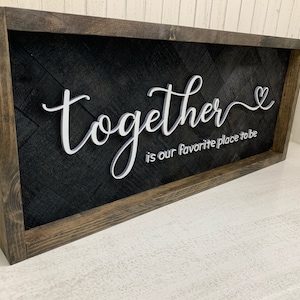 以下が含まれることがあります： 黒い背景に白い文字で「together is our favorite place to be」と書かれた、木製の額縁付きの看板。小さなハートのマークも付いています。