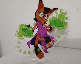 May include: An acrylic standee featuring a cartoon lynx character with brown fur, black ear tufts, and green hands. The character wears a purple dress and is surrounded by green pixelated energy effects on a clear, die-cut acrylic base.