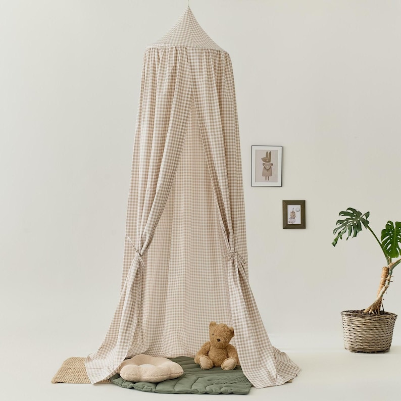 Pu&ograve; includere: Una tenda a baldacchino beige e bianca a quadri vichy con un orsacchiotto di peluche seduto all'interno. La tenda &egrave; realizzata in un tessuto morbido e leggero, perfetta per creare uno spazio accogliente e giocoso per i bambini.