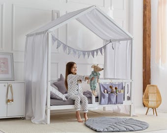 May include: White wooden canopy bed frame with a white sheer canopy and a gray and white patterned bedspread. A young girl is sitting on the bed with a stuffed animal. There are gray and white checkered flags hanging from the canopy.