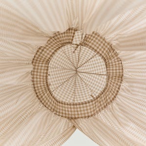 Pu&ograve; includere: Un baldacchino in tessuto gingham marrone e bianco con un'apertura circolare nella parte superiore. Il tessuto &egrave; raccolto attorno all'apertura, creando un effetto arricciato.