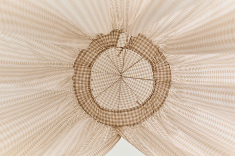 Pu&ograve; includere: Un baldacchino in tessuto gingham marrone e bianco con un'apertura circolare nella parte superiore. Il tessuto &egrave; raccolto attorno all'apertura, creando un effetto arricciato.