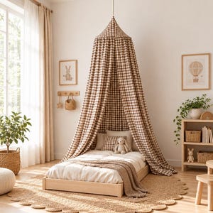 May include: A brown and white gingham canopy hangs from the ceiling over a low wooden bed frame. The bed is dressed in white bedding with a matching gingham pillow and a plush toy. The canopy creates a draped tent effect over the sleeping area.