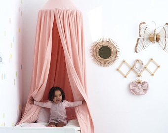 Puede incluir: Una cama con dosel rosa con marco blanco y el texto "Le Soleil". La habitación está decorada con una almohada en forma de estrella y una alfombra en forma de hoja. Una mariposa decorativa y un espejo cuelgan de la pared.
