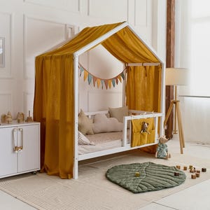 May include: White wooden house-shaped bed frame with a yellow canopy and a green leaf-shaped rug. The bed has a white mattress and a white and gray patterned bedding. There are colorful flags hanging from the top of the bed frame.
