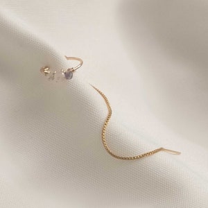 Könnte beinhalten: Ein zarter goldener Kettenohrring mit einem kleinen Cluster aus weißen und violetten Edelsteinen.