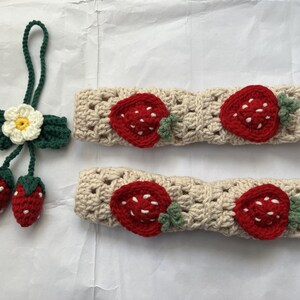 May include: Two beige crocheted headbands with strawberry designs. Each headband has three red strawberries with green leaves.