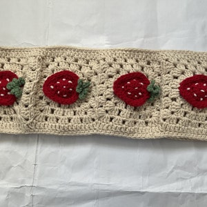 May include: A crocheted headband with a beige background and four red strawberry appliques. Each strawberry has green leaves.