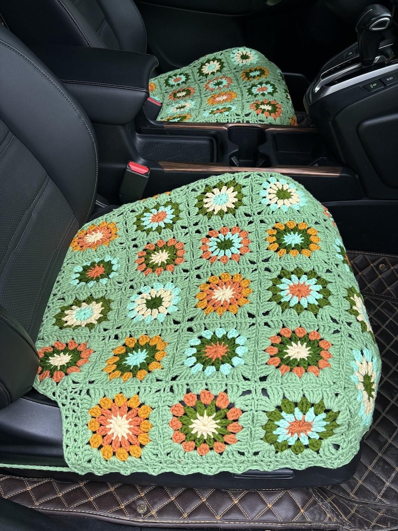 Pu&ograve; includere: Una fodera per sedile auto in crochet verde con un motivo floreale in tonalit&agrave; arancio, giallo, verde e blu.
