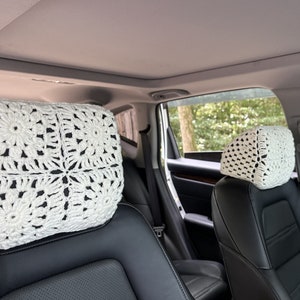May include: Two white crocheted headrest covers for car seats. The covers are made with a square pattern and have a delicate, lacy look.