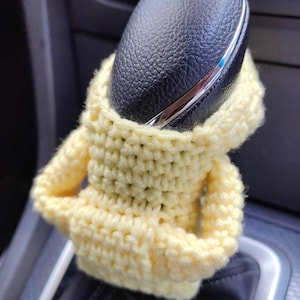 May include: A yellow crocheted hoodie covering a black leather car gear shifter.