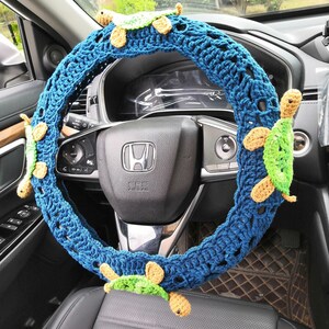 May include: A blue crocheted steering wheel cover with four green and yellow crocheted turtle embellishments.