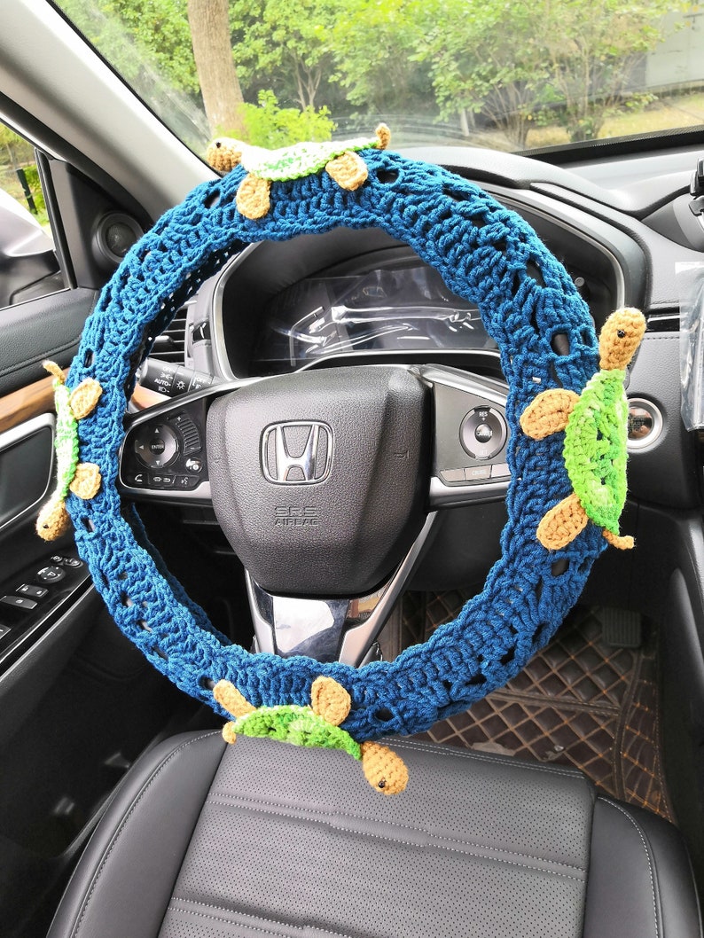May include: A blue crocheted steering wheel cover with four green and yellow crocheted turtle embellishments.