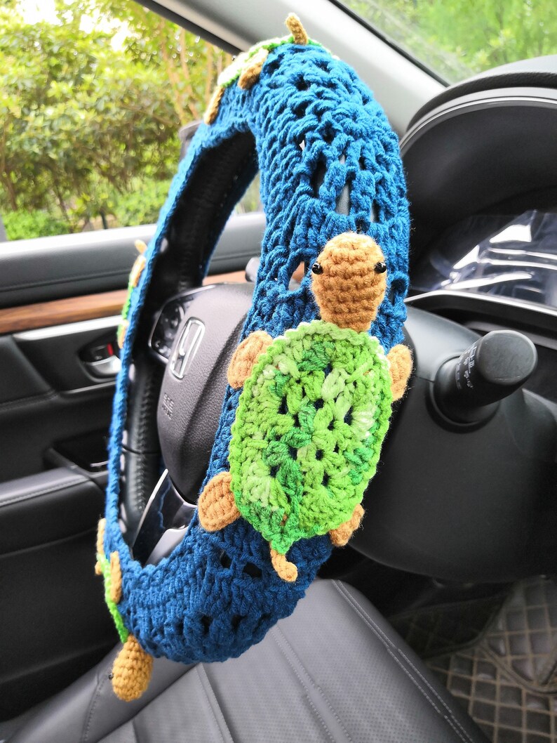 May include: A blue crocheted steering wheel cover with a green and brown crocheted turtle design.