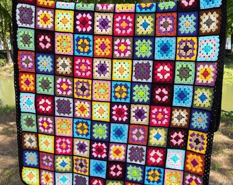 Pode incluir: Uma manta de crochê colorida com uma borda preta. A manta é feita de muitos quadrados, cada um com uma cor e um padrão diferente.