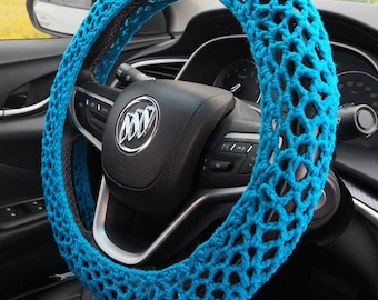 May include: A bright blue crocheted steering wheel cover. The cover is made of a thick, textured yarn and has a honeycomb pattern.