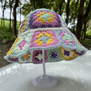 May include: A crocheted bucket hat with a colorful patchwork design featuring squares in shades of pink, purple, yellow, and green.