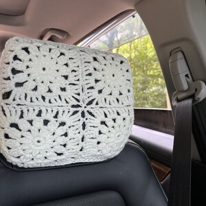 May include: White crocheted headrest for a car seat. The headrest is made of a delicate, lacy pattern and is designed to provide comfort and support.
