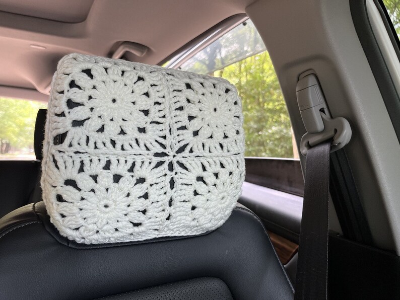 May include: White crocheted headrest for a car seat. The headrest is made of a delicate, lacy pattern and is designed to provide comfort and support.