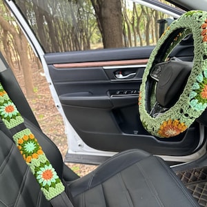 Pu&ograve; includere: Un coprivolante e un copri cintura di sicurezza abbinati, all'uncinetto in verde, giallo e arancione. Le coperture presentano un motivo floreale.