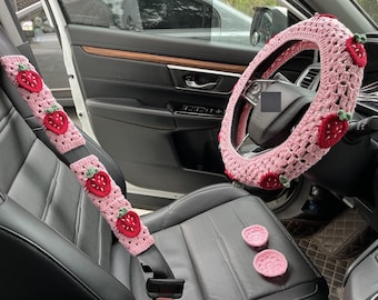 May include: A pink crocheted steering wheel cover with strawberry accents, a pink crocheted seatbelt cover with strawberry accents, and two pink crocheted coasters.