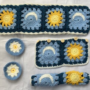 May include: A set of crocheted items in blue, white, and yellow. The set includes a headband, a square, two small circles, and a long rectangle. The items are all made with a granny square stitch and feature a sunflower design.