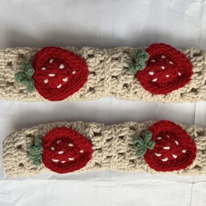 May include: Two beige crocheted headbands with red and green strawberry appliques. Each headband has a single strawberry with white stitching for the seeds.