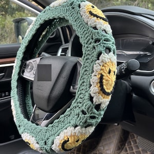 Puede incluir: Funda de volante de crochet verde con caritas sonrientes amarillas.