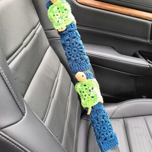 May include: A blue and green crocheted car seatbelt cover with a turtle design.