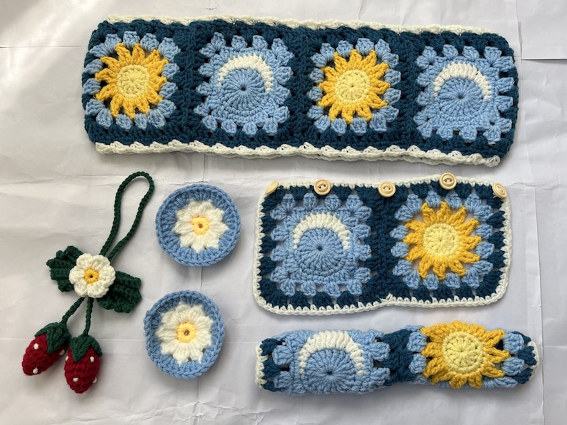May include: A set of crocheted items in blue, white, and yellow. The set includes a headband, a pair of coasters, and a long crocheted piece. The crocheted pieces feature a flower design.