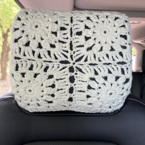 May include: White crocheted headrest cover with a floral pattern. The cover is made of a soft, white yarn and is perfect for adding a touch of elegance to any car interior.