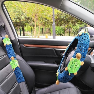 May include: A blue and green crocheted steering wheel cover with a turtle design. A matching blue and green crocheted seatbelt cover with a turtle design is also visible.