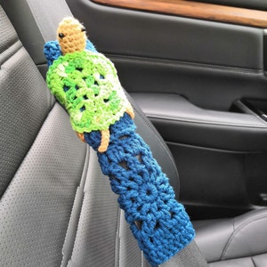 May include: A crocheted blue and green turtle seatbelt cover. The turtle has a brown head and black eyes.