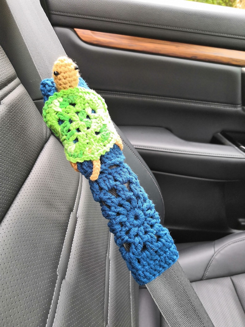 May include: A crocheted blue and green turtle seatbelt cover. The turtle has a brown head and black eyes.