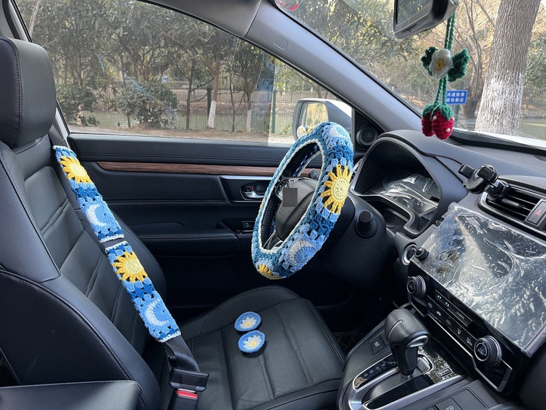 May include: A car interior with crocheted seatbelt covers, a steering wheel cover, and two small crocheted coasters. The covers are blue and yellow with a sun and moon design.