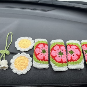 May include: A set of crocheted flower decorations in pink, red, green, and white. The flowers are arranged in a row on a black surface. There are also two smaller crocheted flowers with yellow centers.