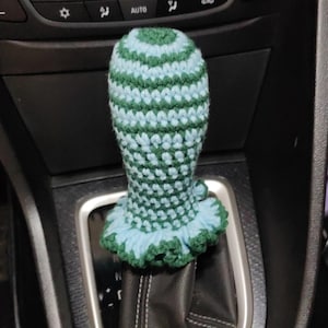 Pode incluir: Um botão de câmbio de marchas de crochê verde e azul com uma parte inferior franjada.