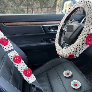 May include: A white crocheted steering wheel cover with red strawberry designs. The cover is also available in seatbelt covers and small coasters with the same design.